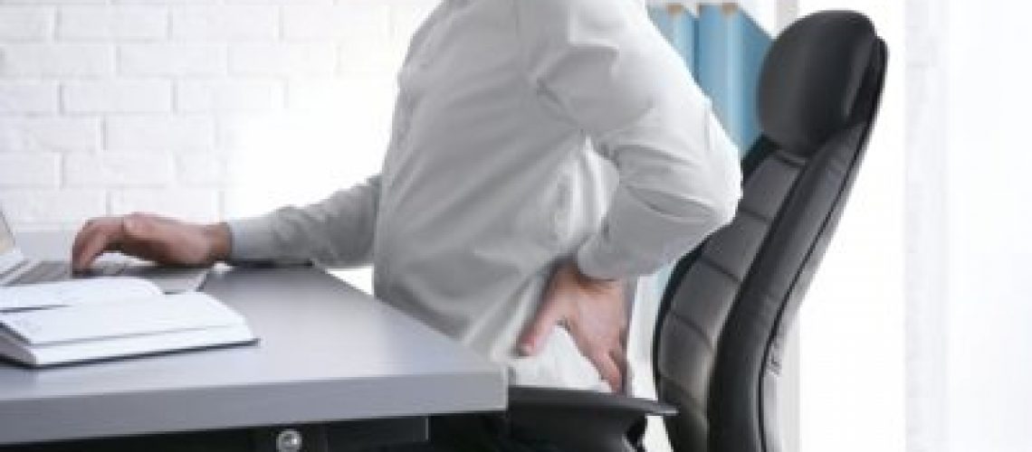 Posture concept. Man suffering from back pain while working with laptop at office